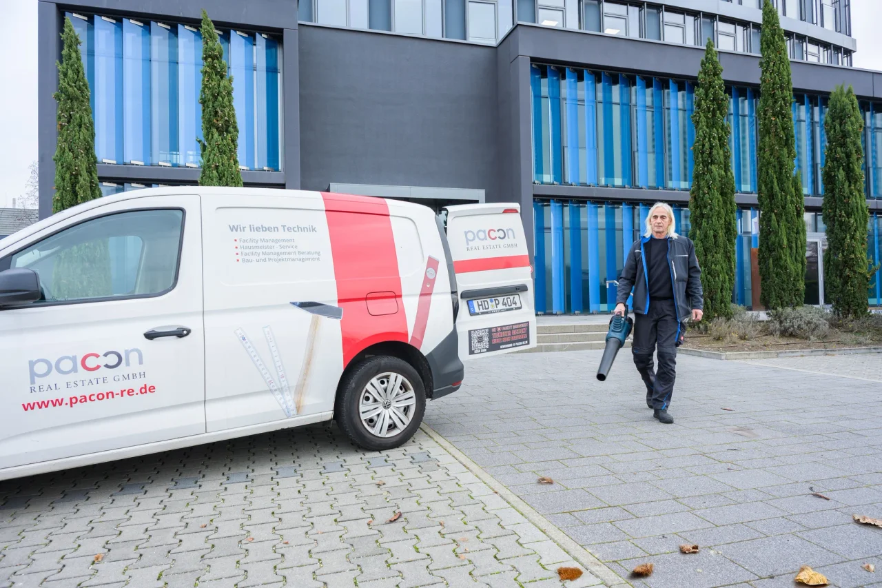 pacon-Servicetechniker mit Laubbläser vor einem Bürogebäude, daneben ein pacon-Servicefahrzeug